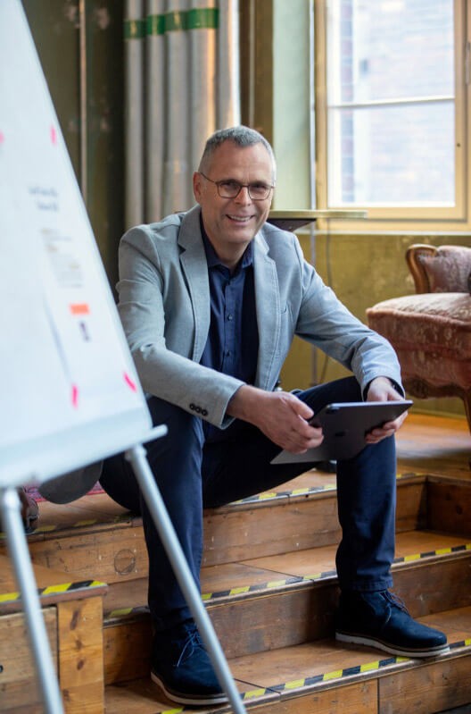 Stefan Mierzowski mit Tablet in der Hand sitzend auf Treppe